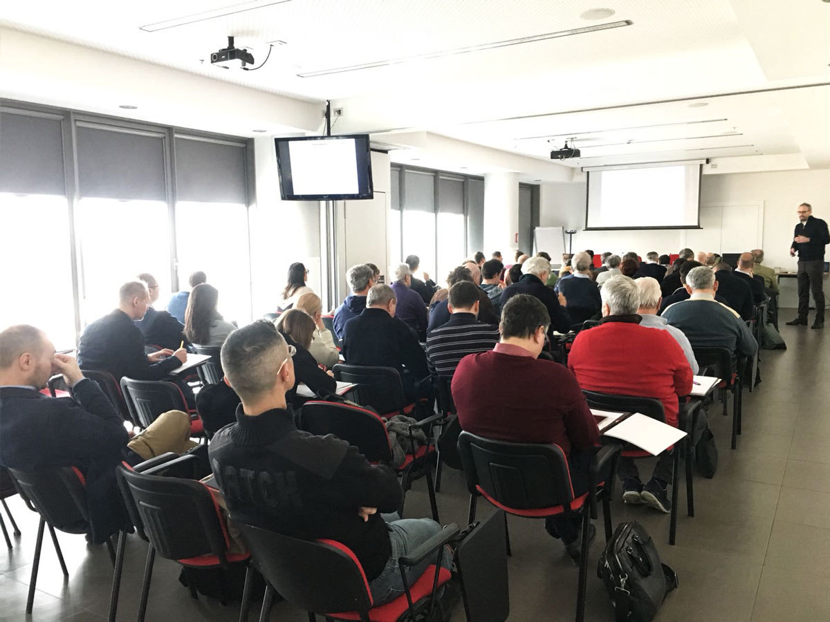 Sala riempita da persone che ascoltano il relatore ad un convegno di lavoro